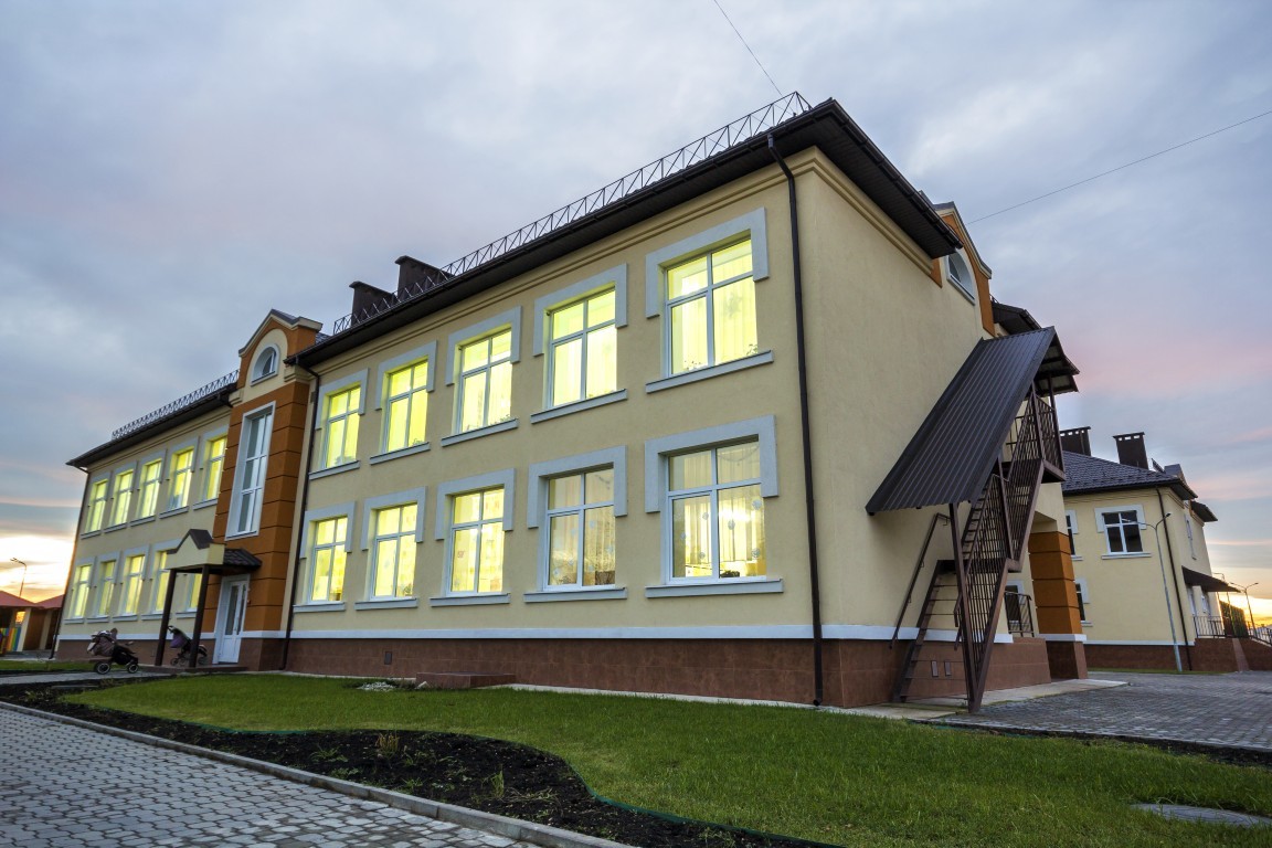 New modern two storied kindergarten preschool building,green grassy lawn and paved sidewalks on blue sky copy space background. Architecture and development concept.