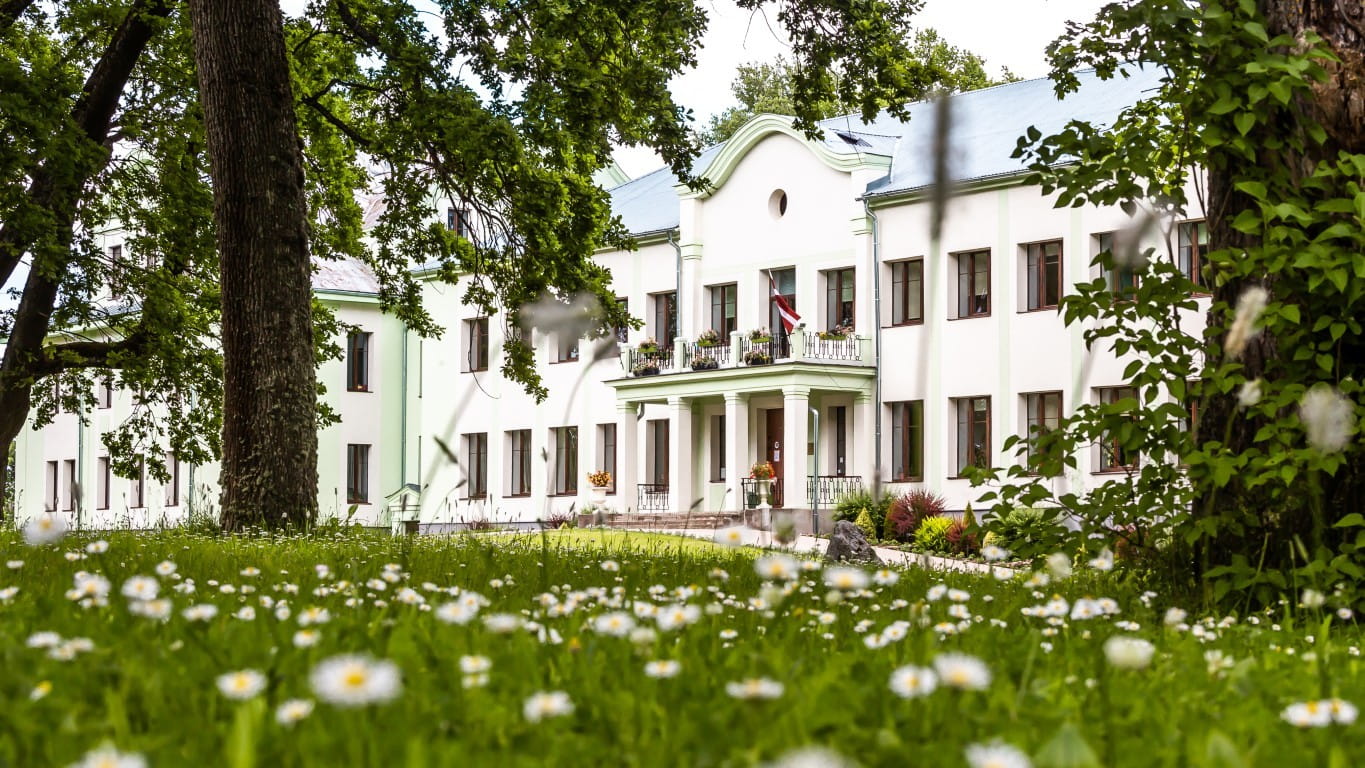 White two story building with balcony columns amid tall trees (1)